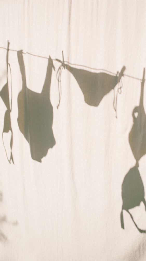 Swimsuits on a washing line, seen as soft shadows through a sunlit cream curtain